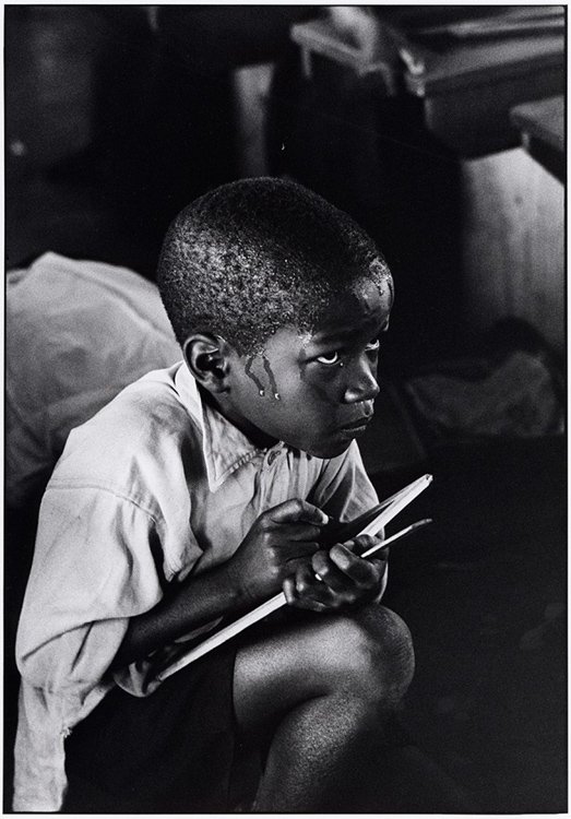 Ernest Cole - Earnest boy squats on haunches and strains to follow lesson in heat of packed classroom, South Africa