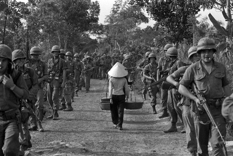 Henri Huet - With apparent disregard for the columns of U.S. Marines on the road, South Vietnamese natives walk the center, Vietnam 1968