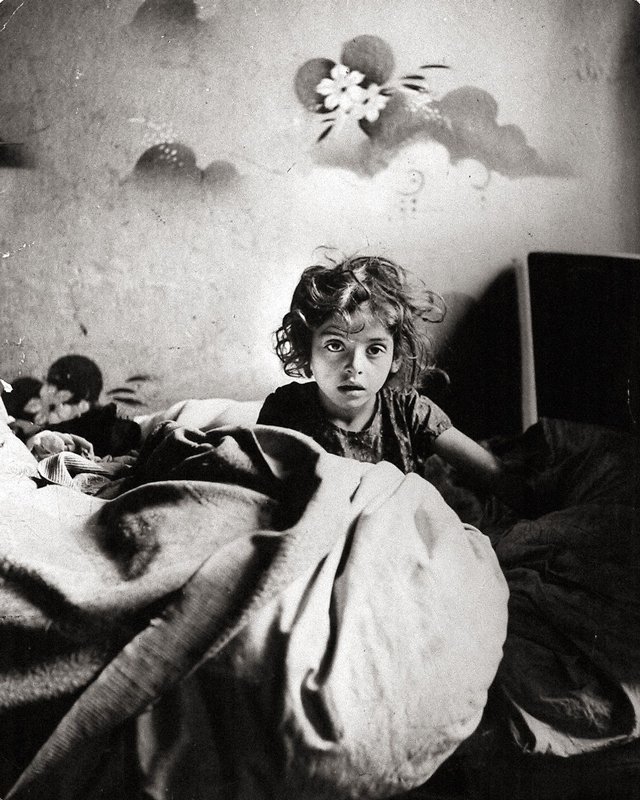 Roman Vishniac - Sara, sitting in bed in a basement dwelling, with stencilled flowers above her head, Warsaw 1935