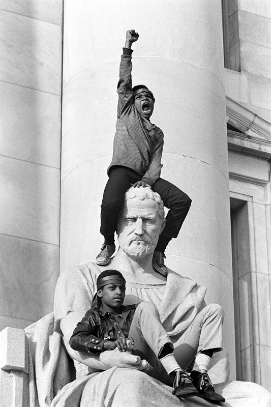 Stephen Shames - Boy gives raised fist salute as he and a friend sit on a statue in front of the New Haven, Connecticut, USA 1970