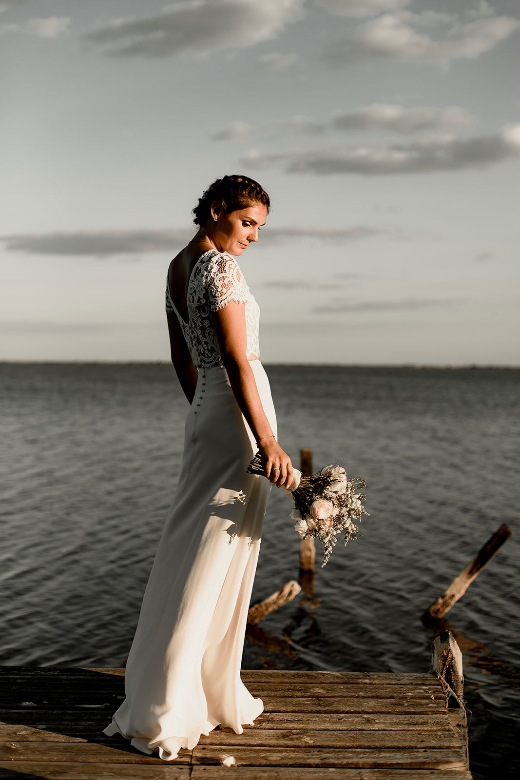Séance photo de la mariée au bord de la mer coiffure chignon bas et flou avec fleurs